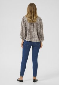 Animal print blouse in beige and brown, featuring a relaxed fit, puffed sleeves, and gathered detailing at the back, paired with blue skinny jeans.