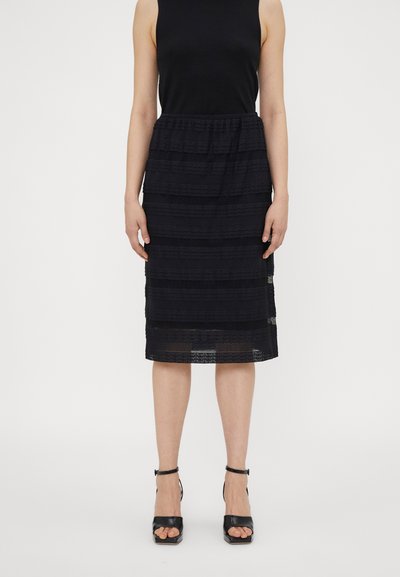 Svart midi skjørt med teksturert stripemønster, elastisk midjebånd og lagdelt design. Kombinert med svarte høyhælte sandaler.