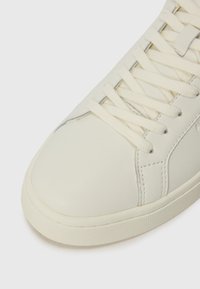 Witte leren sneaker met platte veters, ronde neus en gestructureerde rubberen zool. Beschikt over een subtiele naaddetail langs de zijkant.