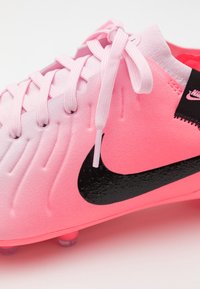 Futbalová obuv s gradientom v ružovej farbe, štruktúrovaným povrchom, čiernym logom Nike a ružovými šnúrkami. Obsahuje tvarovanú pätu a priehľadné kolíky.