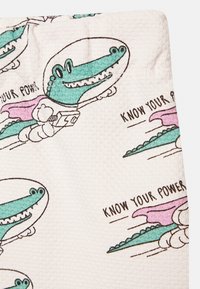 Toalha de tecido com um fundo texturizado branco, apresentando crocodilos verdes divertidos com capacetes espaciais, capas cor-de-rosa, e a frase "CONHECE O TEU PODER".