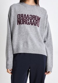 Maglione grigio lavorato a maglia con orlo e polsini a coste, con il testo "Norgaad" in un bordeaux scuro sulla parte anteriore. Texture morbida e vestibilità rilassata.