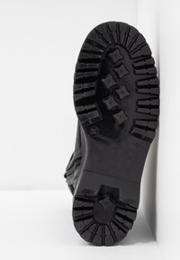 Suola in gomma nera con un motivo di battistrada robusto, caratterizzato da profonde scanalature ed elementi di trazione esagonali per una migliore aderenza.