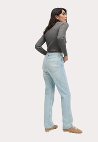 Jeans azzurri a vita alta con una vestibilità comoda, abbinati a un top lungo a maniche rigate di colore grigio scuro. Scarpe da ginnastica in suede marrone completano il look.