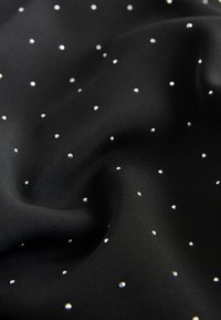 Melns audums ar maziem, vienmērīgi izkārtotiem baltiem rhinestones, rādot maigas locījumus un smalku tekstūru.