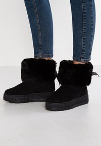Svarta ankle boots i mocka med en faux fur-kant, strukturerad gummisula och mönstrad dragrem bak.