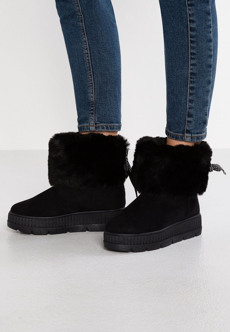 Svarta ankle boots i mocka med en faux fur-kant, strukturerad gummisula och mönstrad dragrem bak.