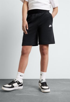 Pantalones cortos deportivos negros con cinturilla elástica y bolsillos laterales, combinados con zapatillas negras y blancas y calcetines blancos con el logo de Nike.