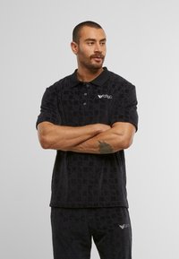 Black, textured polo shirt with short sleeves and a buttoned collar. Features a subtle pattern and a logo on the chest.