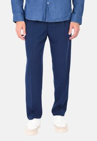Pantaloni blu navy con una texture liscia, caratterizzati da una vestibilità dritta e leggere pince, abbinati a sneakers bianche e a una camicia di denim.