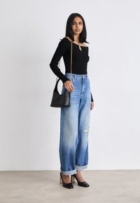 Top noir à manches longues côtelé avec un détail en trou de serrure, associé à un jean large taille haute en délavé clair. Accentué par un sac à main noir et des escarpins pointus.