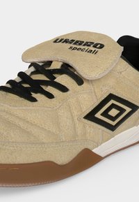 Μπεζ σουέτ αθλητικό παπούτσι Umbro Speciali με μαύρα κορδόνια, μαύρο δίπλο διαμαντένιο λογότυπο και καφέ λεπτομέρεια λαστιχένιας σόλας σε λευκό φόντο.