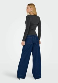 Tætsiddende sort langærmet top parret med brede blå denimjeans. Jeansene har to baglommer og kontrasterende syninger.