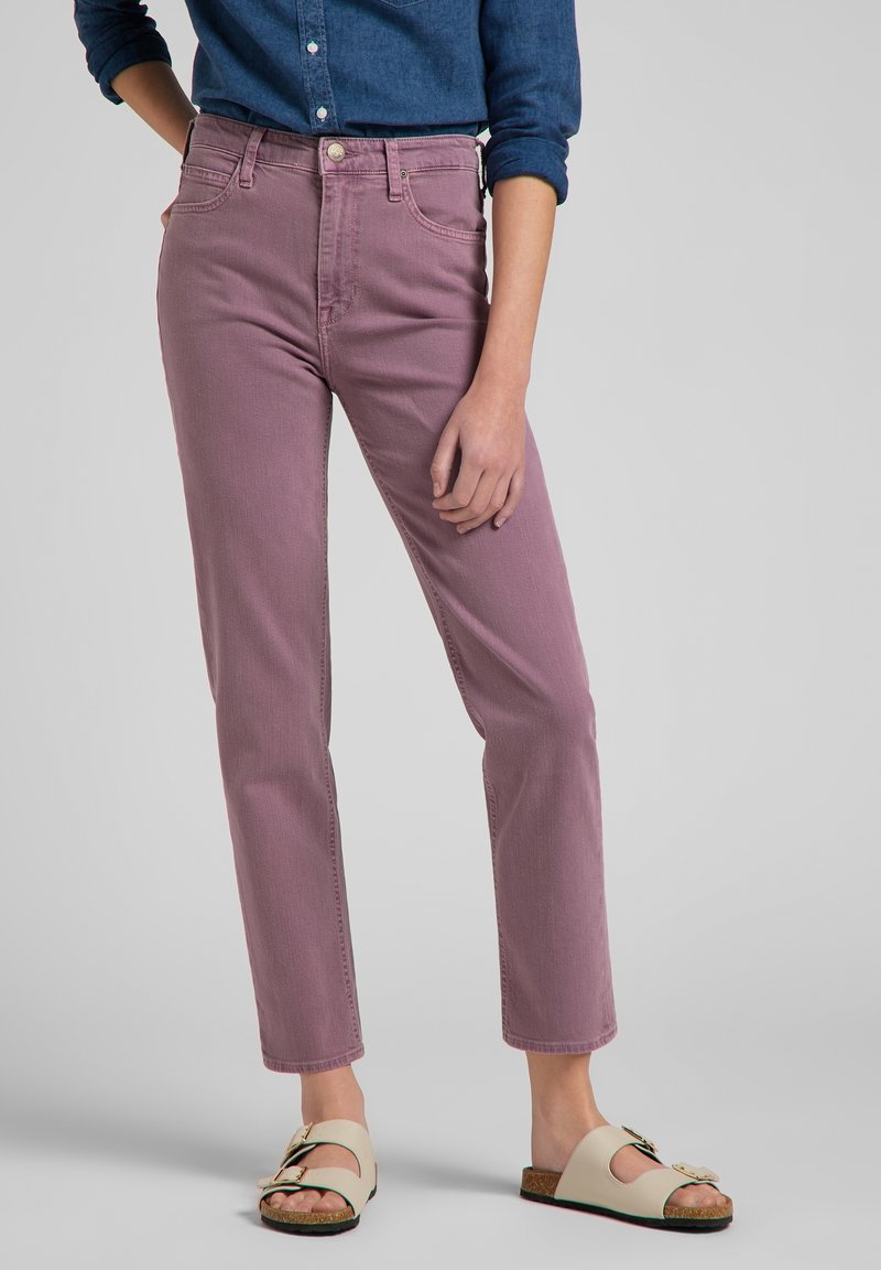 Personne portant un jean taille haute mauve à jambes droites, une chemise bleu foncé à manches longues retroussées et des sandales ouvertes beige avec des boucles.
