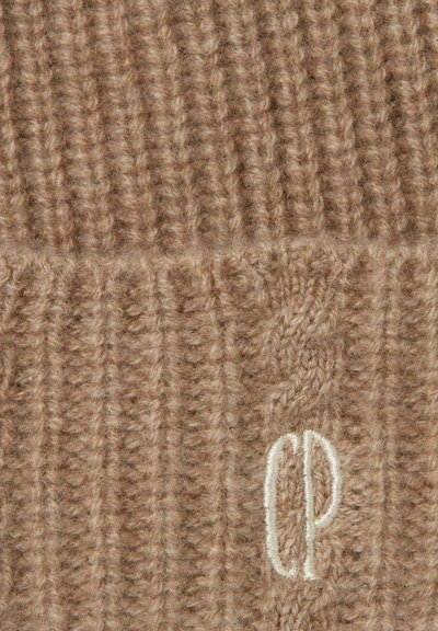 Cappello a maglia beige con texture a coste. Tra i dettagli spicca un logo ricamato "CP" in bianco. Materiale in lana morbida con un aspetto accogliente.
