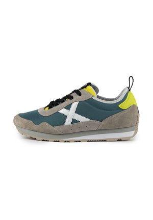 Zapatilla azul y gris con acentos blancos, materiales de suede texturizado y tela, cordones negros, detalles amarillos y suela gris claro.