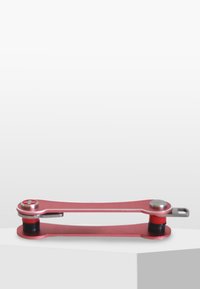 Outil multifonction en métal rouge avec une forme mince et allongée, doté d'une accentuation argentée, de poignées en caoutchouc noir et d'un point de pivot pour l'ajustement.