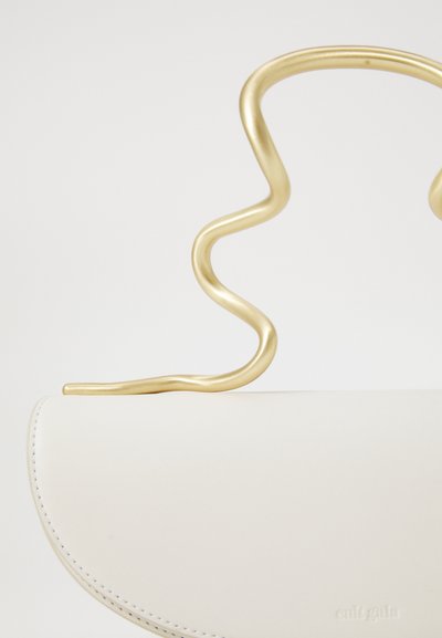 Hvid læderhåndtaske med et skulpturelt bølget guldmetalhåndtag mod en ensfarvet baggrund, der har diskret præget branding.