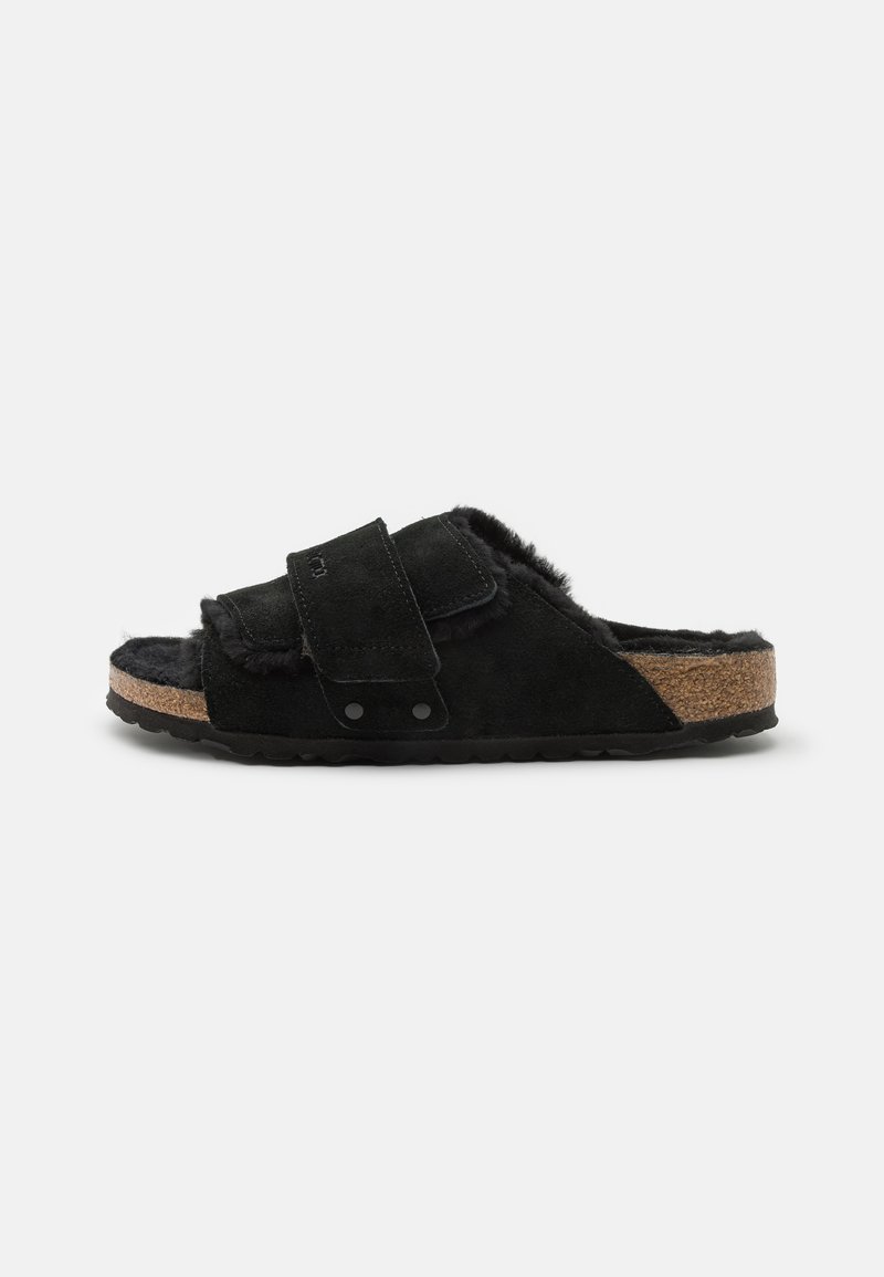 Black suede slide sandal with adjustable strap, soft fur lining, cork footbed, and textured rubber sole. Accented with black hardware.