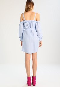 Abito azzurro chiaro scollato con maniche a sbuffo lunghe, vita cintrata e cintura. Il tessuto appare liscio, semi-attillato sopra il ginocchio. Stivali rosa con tacco.