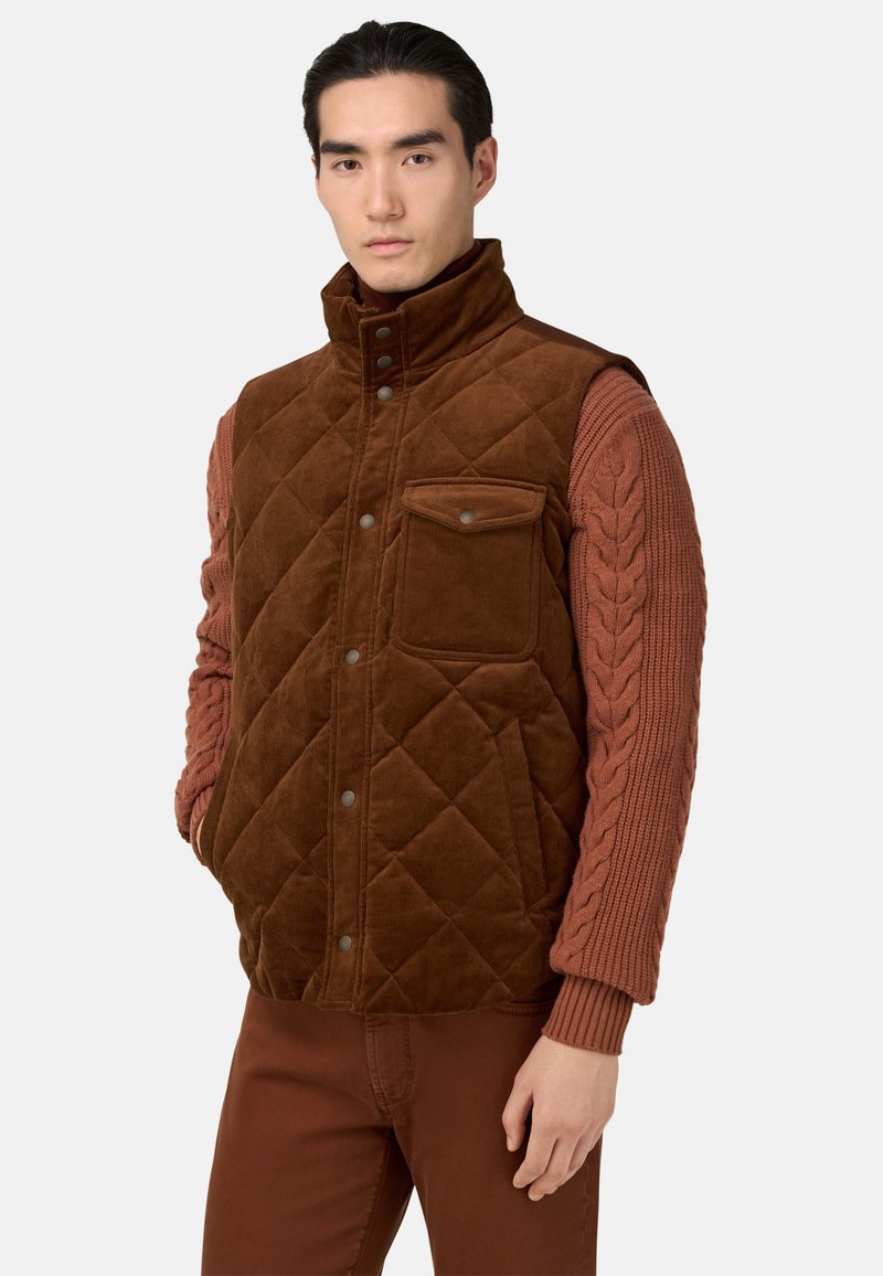 Gilet in corduroy marrone con trapuntatura a rombi, tasca frontale e colletto alto; presenta maniche in maglia con motivo a trecce di un marrone più scuro.