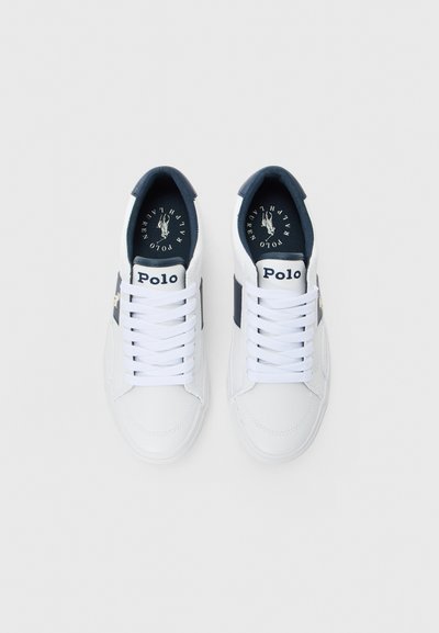 Baskets blanches Polo Ralph Lauren avec doublure de talon bleu marine, rayure sur le côté, et logo "Polo" sur la languette et la semelle intérieure, vues de dessus.