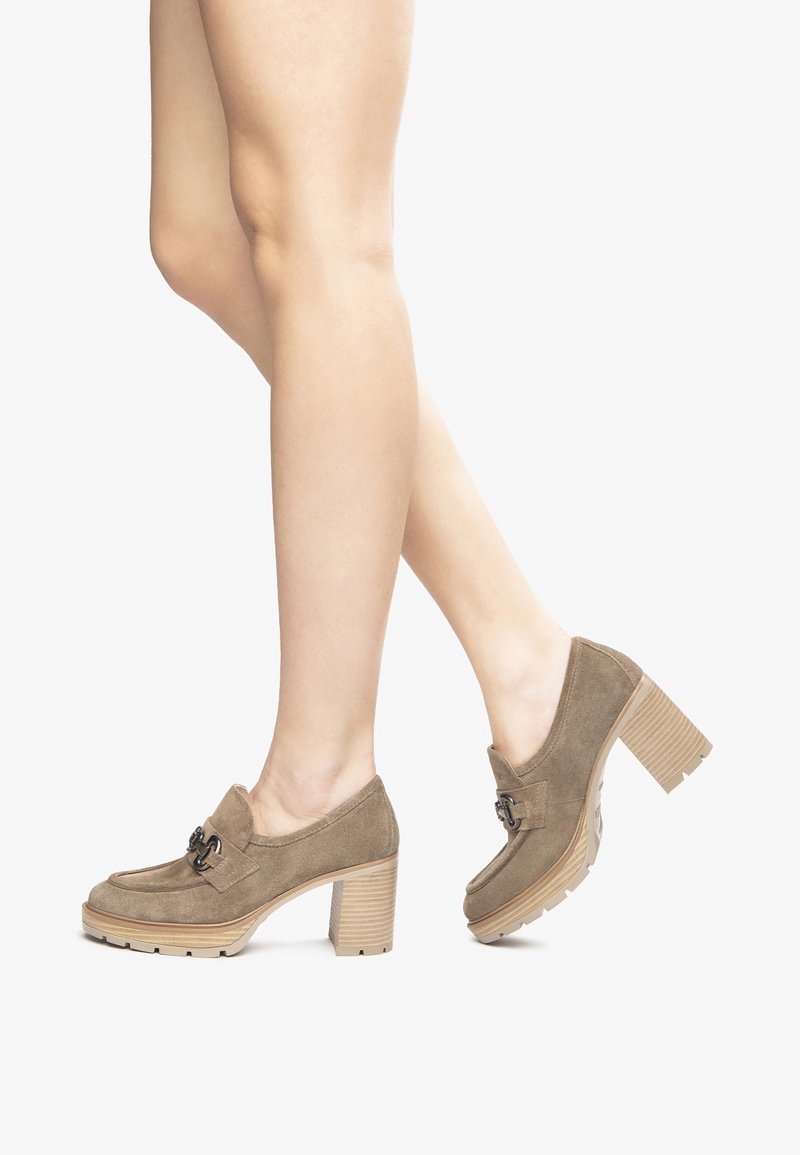 Zapatos de tacón de ante en tono marrón claro con tacón cuadrado y detalles de hebillas decorativas. Suelas gruesas y texturizadas que mejoran la estabilidad y el agarre.