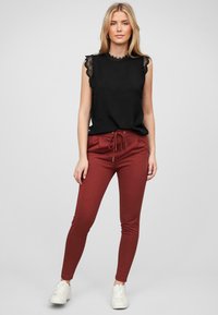 Čierny bezrukávový top s čipkovým lemovaním na pleciach, skombinovaný s burgundskými joggermi s elastickým pásom. Biele topánky dotvárajú outfit.