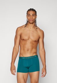 Türkise Boxershorts mit schwarzem Bündchen, auf dem das Logo "JACK & JONES" abgebildet ist. Sitoffensiv, Baumwollmaterial, glatte Textur.