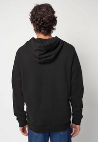 Sudadera negra con capucha de doble capa, mangas largas y corte relajado, hecha de un tejido texturizado. La vista trasera muestra las costuras y detalles de la confección.