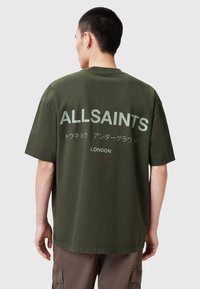 Camiseta de algodón verde oliva con un corte relajado. Presenta un gran texto blanco en la parte posterior: "ALLSAINTS," caracteres japoneses y "LONDRES."