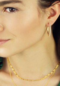 Goldene Creole mit einer Reihe klarer Kristalle, kombiniert mit geschichteten goldenen Ketten. Glatte Oberfläche und glänzende Ausführung.