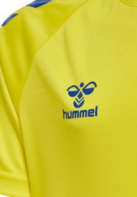 Ljusgul sporttröja i slät tyg, med blå logotyp och detaljer på axeln. Kort ärm och rund halsdesign.