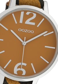 Round OOZOO watch with a brown dial, bold white hour markers, silver hands, and a soft black and brown suede strap.