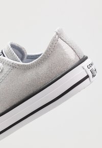 Glitzernder silberner Canvas-Sneaker mit abgerundeter Spitze, weißer Sohle und schwarzem Streifen. Verfügt über Metallösen und ein strukturiertes Obermaterial für zusätzliche Details.