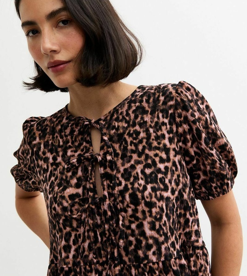 Abito a fantasia leopardata in rosa e nero; maniche a palloncino corte; scollatura a chiave con dettaglio legato; tessuto morbido; silhouette fluida.