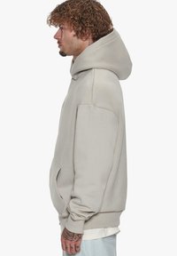 Beige sweatshirt med hætte, løs pasform og forlommer. Har ribbede manchetter og blød stofstruktur. Ingen synlige mønstre eller hardware.