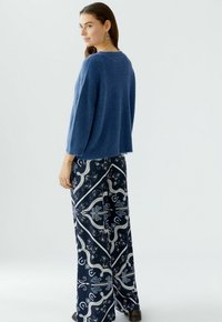 Pull en maille bleu avec une coupe décontractée, associé à un pantalon ample bleu marine orné d'un motif floral et paisley blanc.