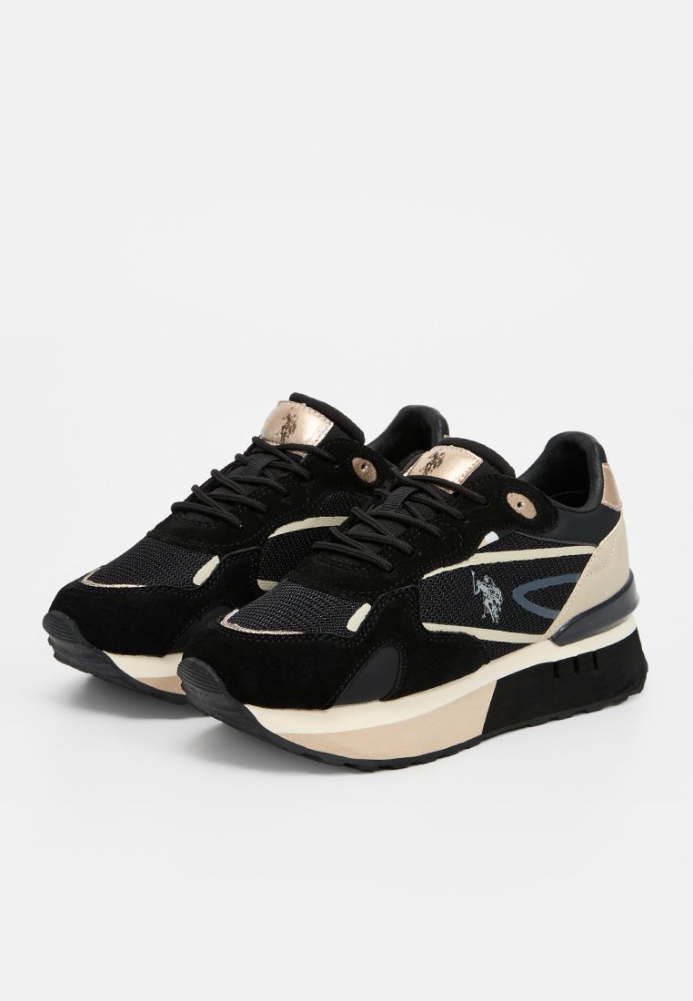 Zapatillas negras con una mezcla de material de ante y malla, con acentos en crema, una lengüeta dorada en el talón y un logo en el lateral. Suela de goma gruesa.