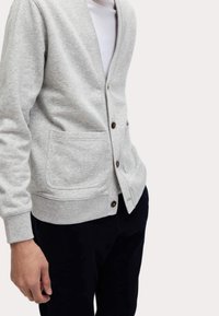 Cardigan grigio realizzato in morbido tessuto, con scollatura a V, maniche lunghe, due tasche frontali e bottoni marroni per la chiusura.