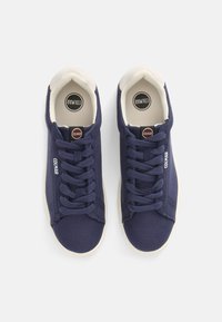 Baskets en toile navy avec semelles en caoutchouc beige, dotées de lacets ronds, de détails de couture subtils et d'un logo sur le côté.
