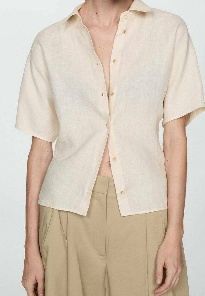 Torse mince portant une chemise à manches courtes beige clair, boutonnée partiellement ouverte, associée à un pantalon ample taille haute de couleur fauve.