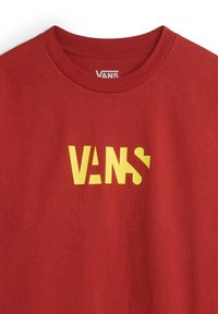 Camiseta de algodón roja con un atrevido logotipo amarillo de "VANS", con un diseño clásico de cuello redondo y mangas cortas. Textura suave con un mínimo de detalles.