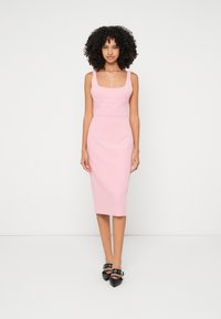 Ružičasta uska midi haljina sa kvadratnim izrezom, bez rukava i jednostavnim šavovima; u kombinaciji s crnim cipelama s oštrim vrhom.