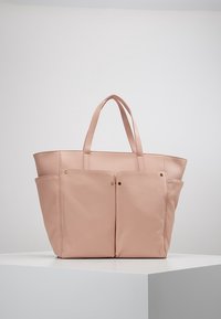 Vaaleanpunainen nahkainen olkalaukku, jossa kaksi etutaskua, kaksinkertaiset kahvat ja kullanväriset metallikoristeet. Sileä pinta, jämäkkä muotoilu.