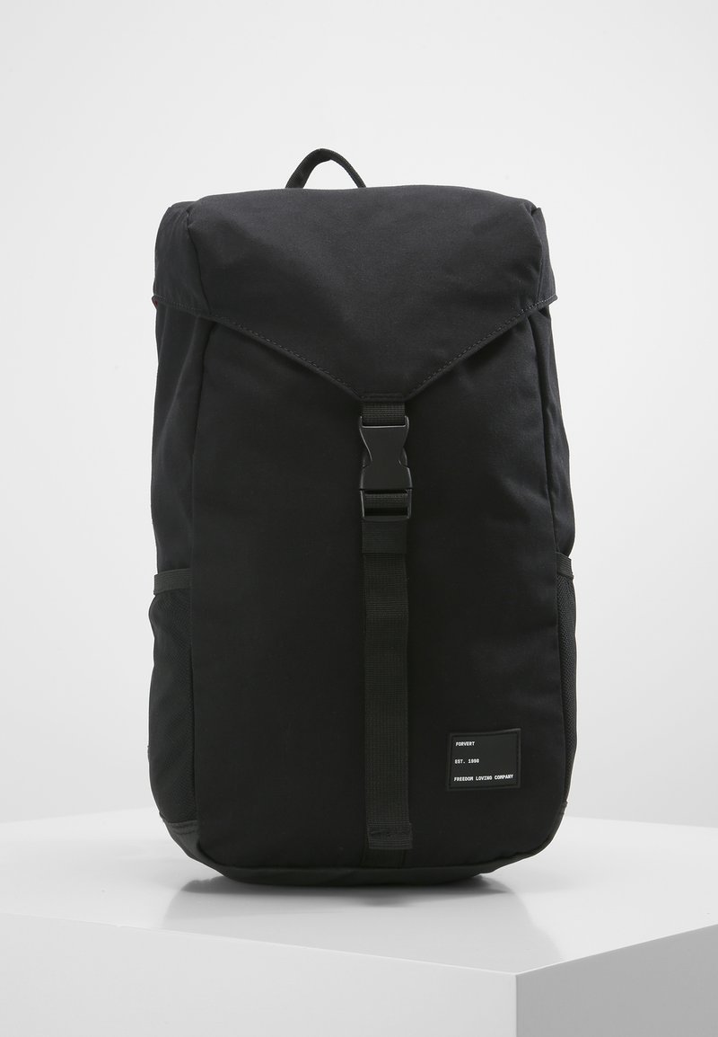 Mochila negra hecha de tela texturizada, con una tapa plegable, correa central con hebilla, bolsillos laterales y una etiqueta en la parte frontal.