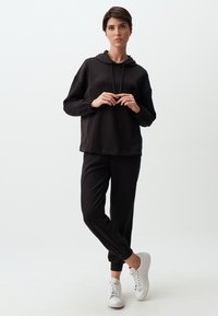 Zwarte pullover hoodie met elastische manchetten, gecombineerd met zwarte tapse sweatpants. Witte sneakers en een minimalistisch ontwerp accentueren de outfit.