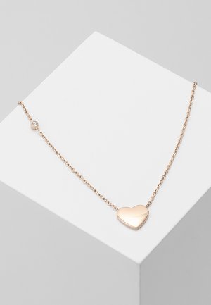 Zarte goldene Halskette mit einem glatten herzförmigen Anhänger und einem kleinen runden Edelstein in der Nähe des Verschlusses, präsentiert auf einer weißen Oberfläche.