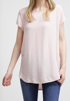 Helles rosa Kurzarmbluse aus fließendem Stoff mit abgerundetem Saum, lockerer Passform und glatter Textur. Kombiniert mit blauen Jeans.