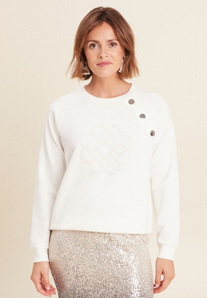 Weißer Sweatshirt mit einem strukturierten, gestickten Knoten-Design auf der Vorderseite, versehen mit drei silbernen Knopf-Akzenten an der Schulter.